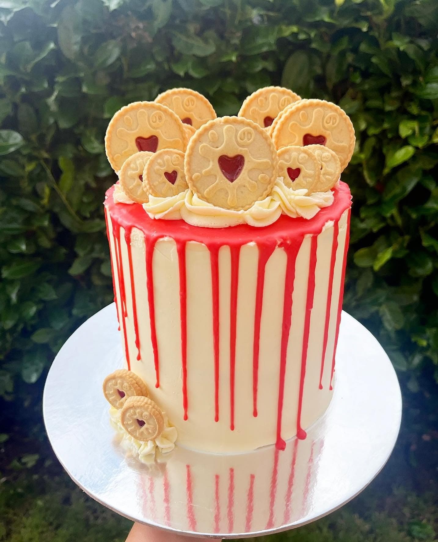 Tall cream cake with red drip and Jammie Dodger biscuit decoration