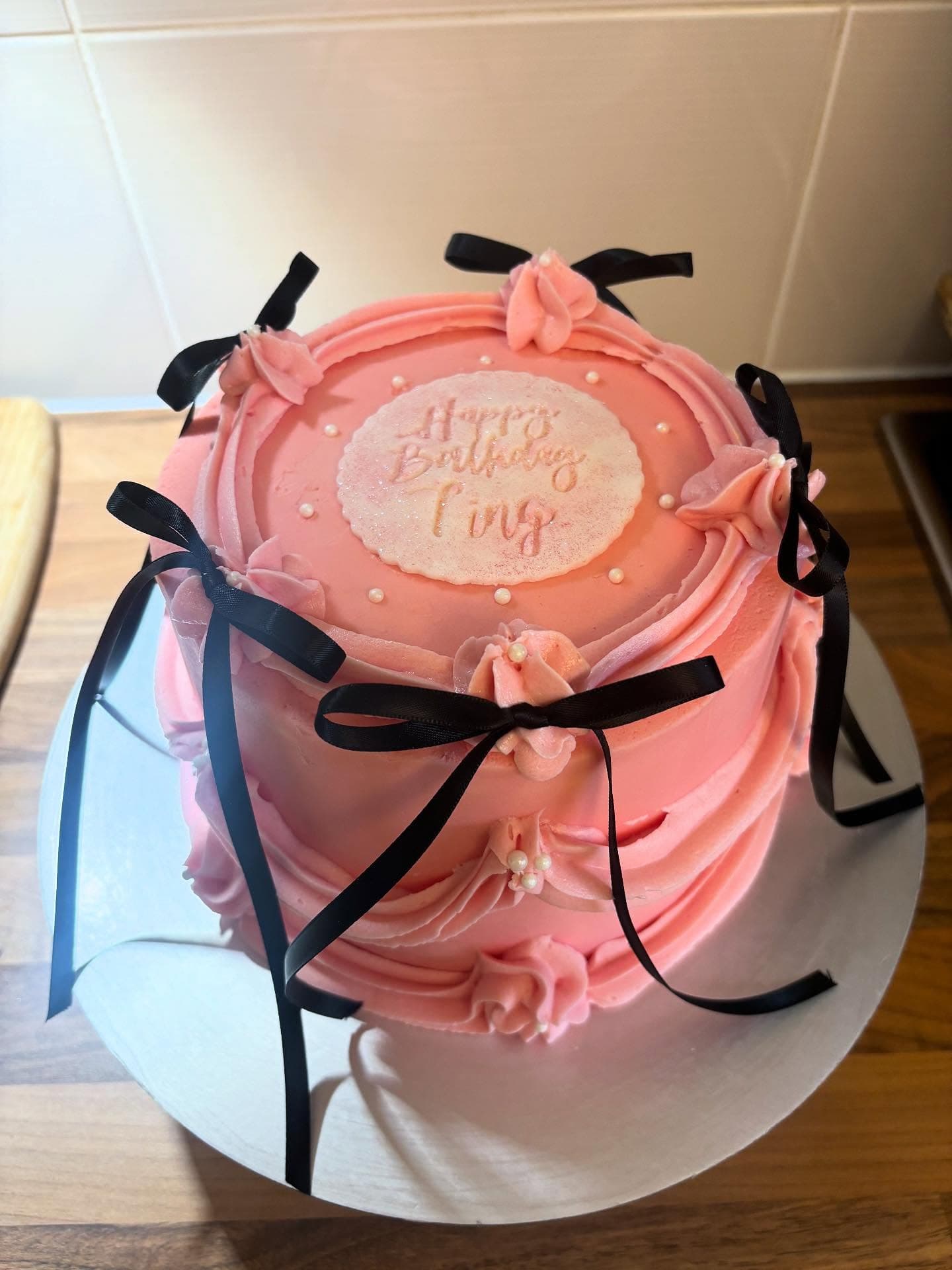 Pink birthday cake with black bow details and piped swags