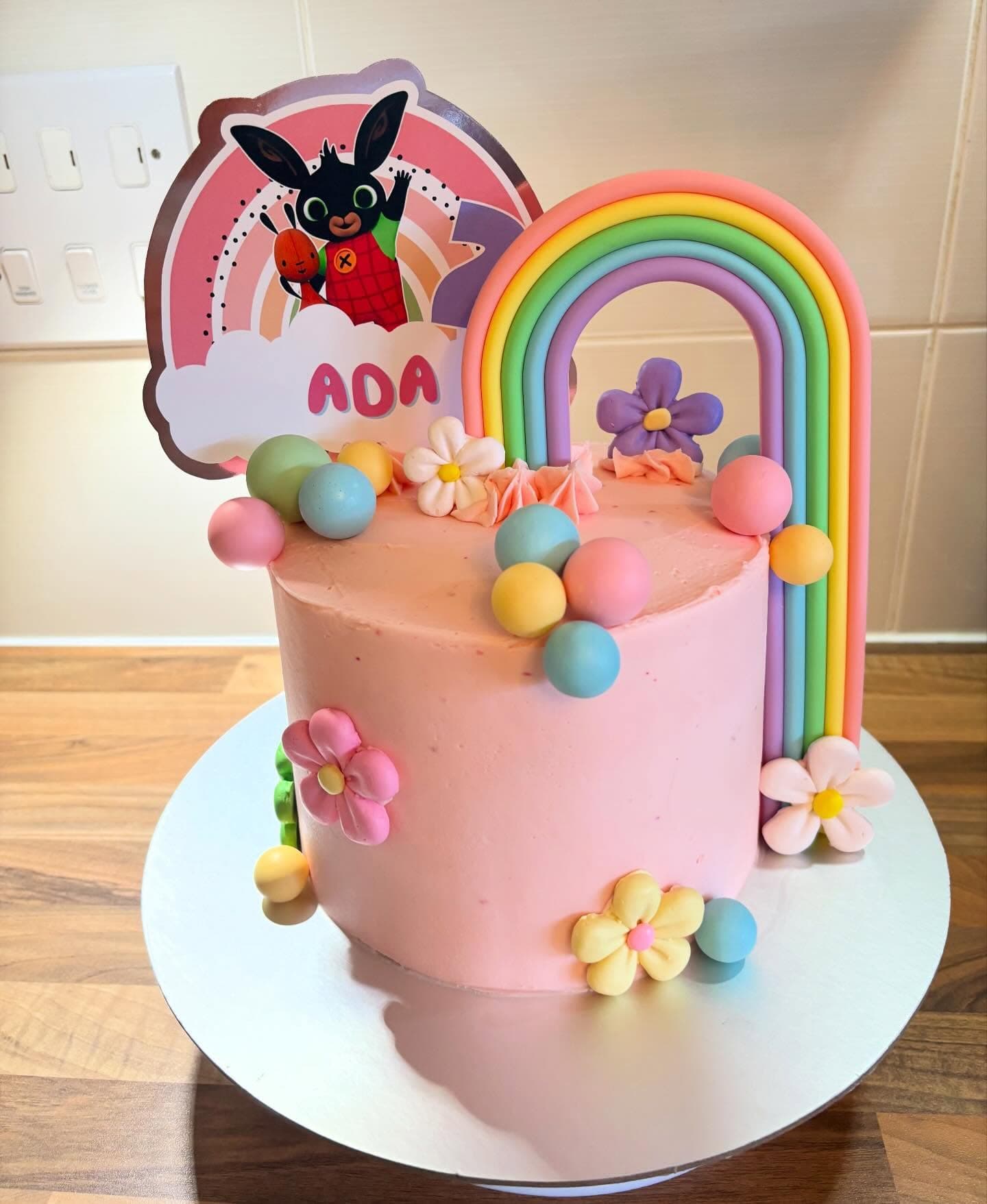 Pastel pink cake with a rainbow topper and flower decorations