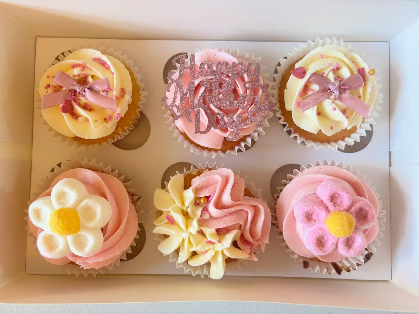 Box of Mother's Day cupcakes decorated with pink bows and flower details