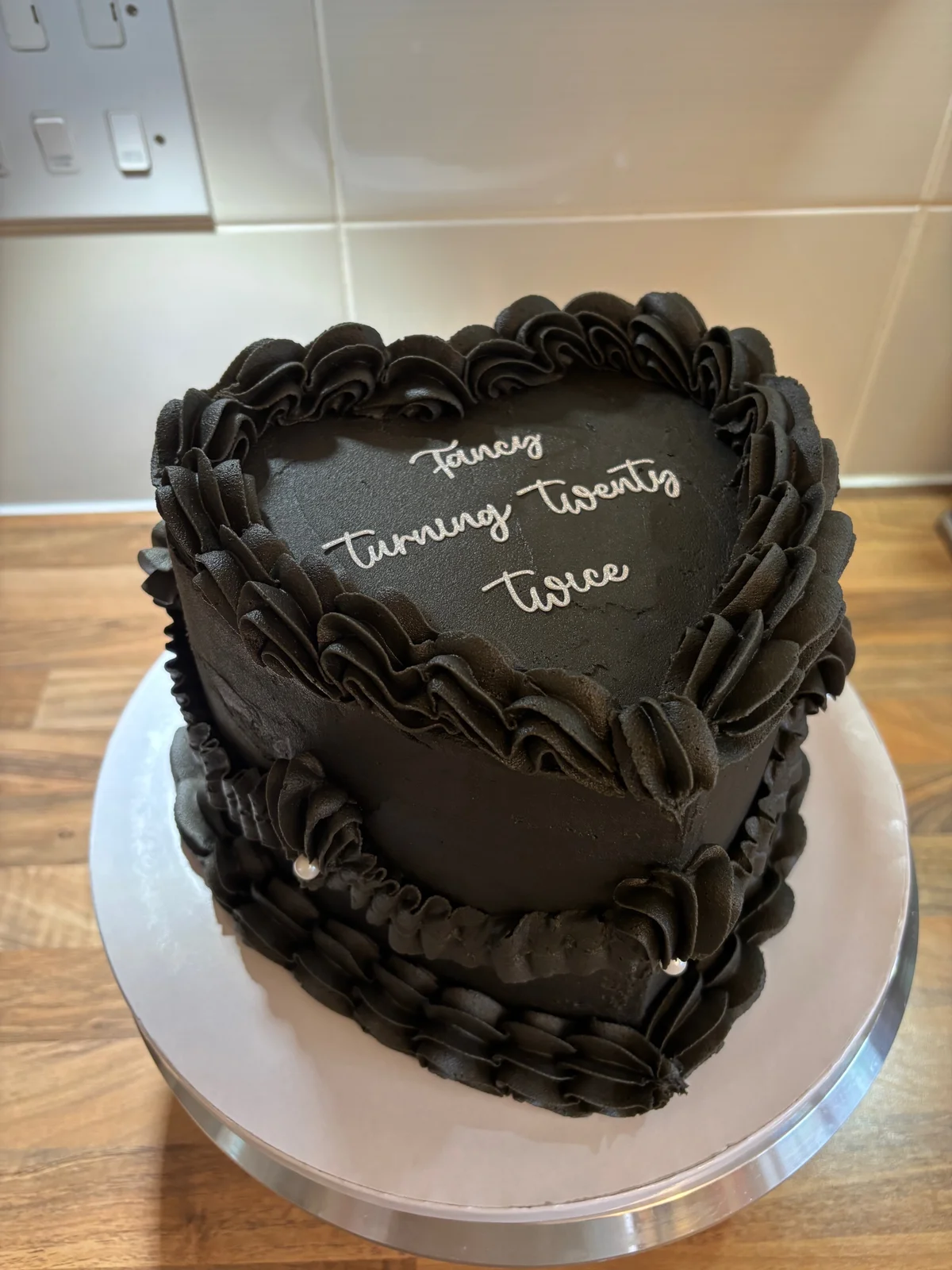 Black heart shaped birthday cake with elaborate piped borders and silver lettering