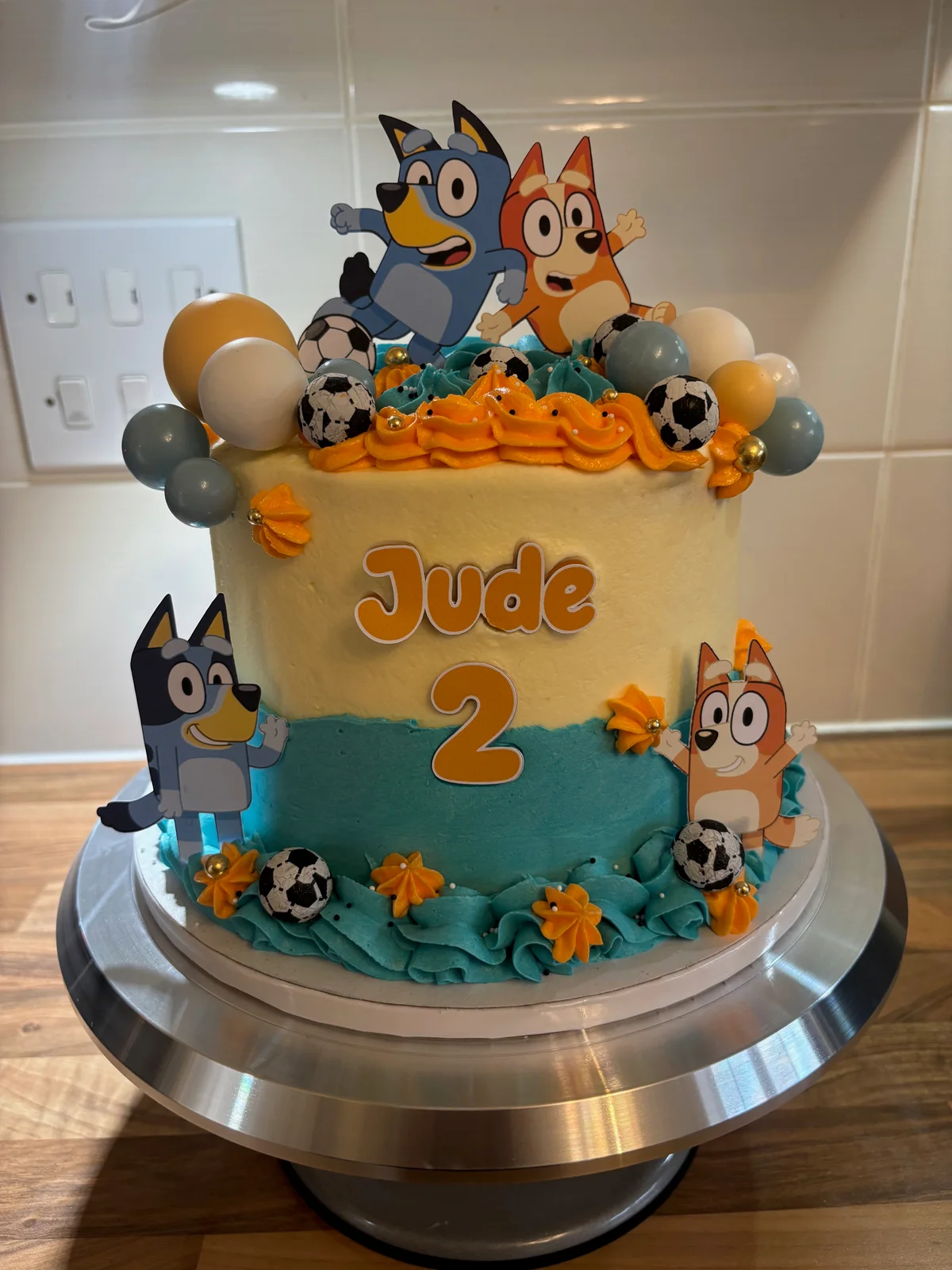 Bluey second birthday cake with blue and orange piping, footballs and character toppers