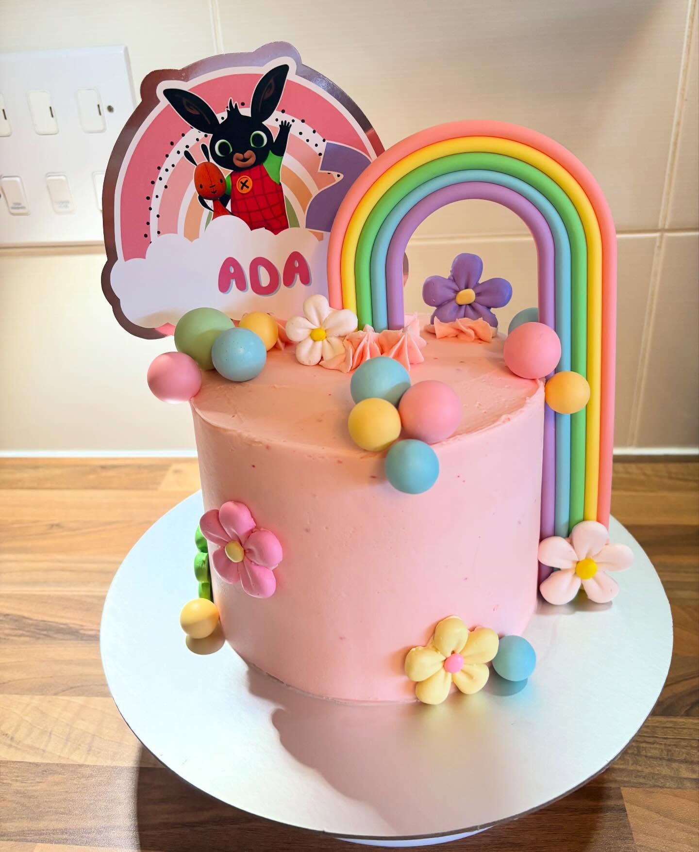 Pastel pink cake with a rainbow topper and flower decorations