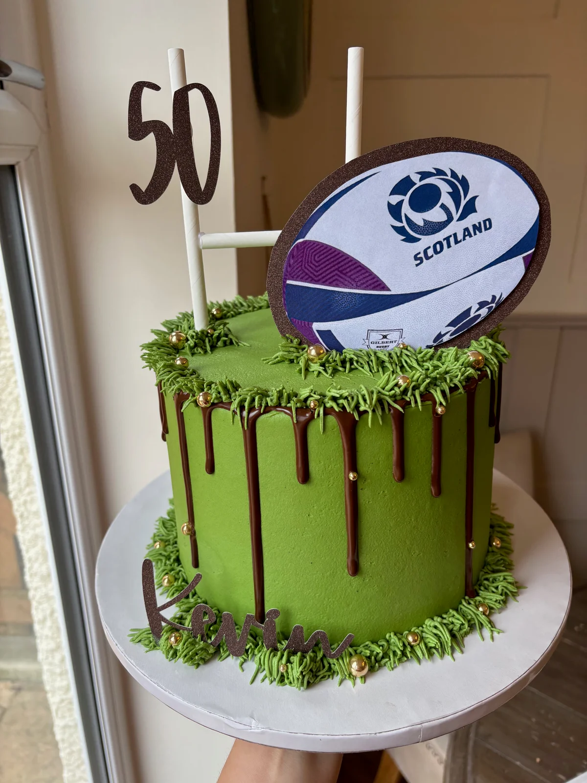 Green Scotland rugby fiftieth birthday cake with chocolate drips, goalposts and a rugby ball topper